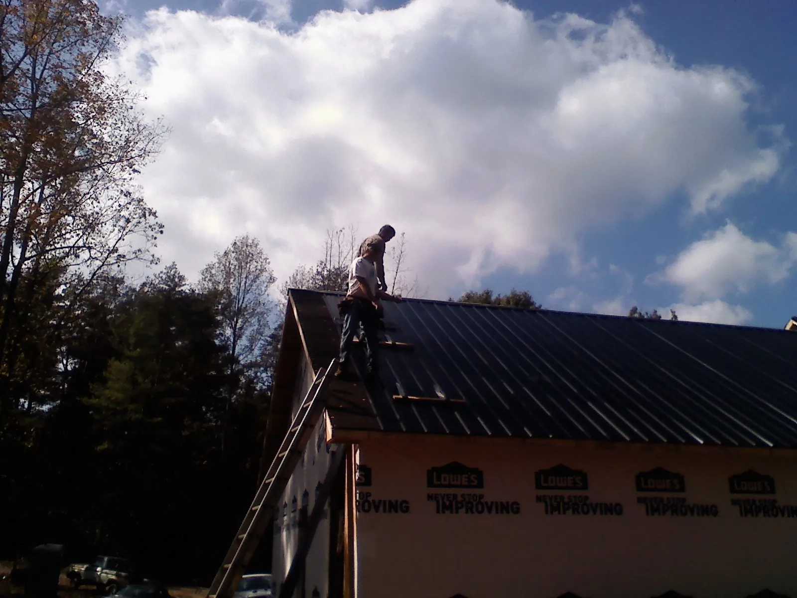 Roofer fastening dark metal panels high against a cloudy sky, from a Roof Inspection job in Rock Island